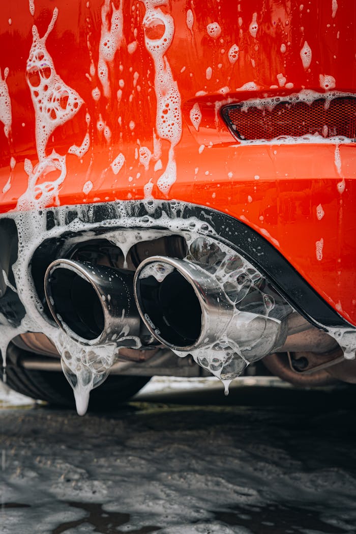 Detailed view of a red sports car exhaust pipe covered in foam at a car wash.