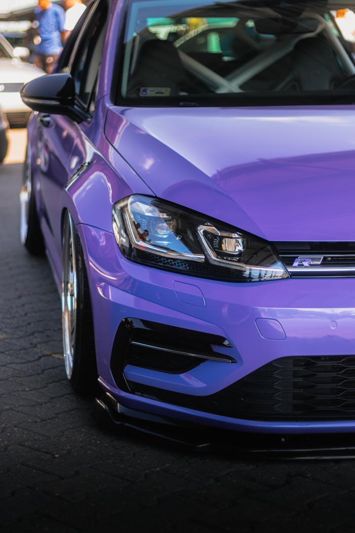 Vertical close-up shot of a modern purple car emphasizing its custom headlights and sleek design.