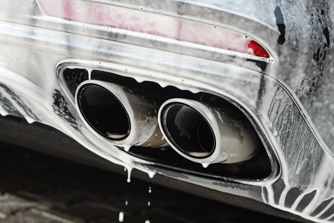 Dual exhaust pipes covered in soap suds during a thorough car wash.