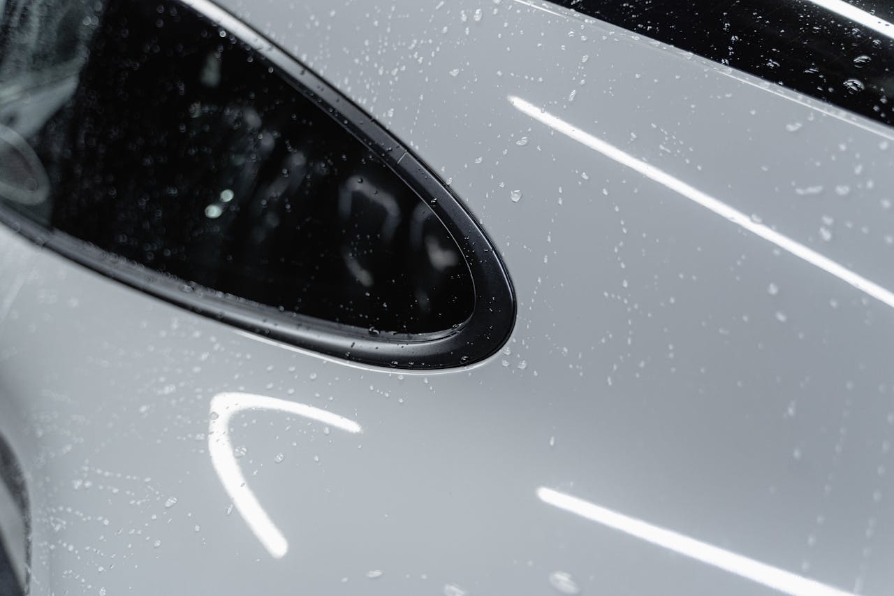 A detailed view of a white car with water droplets after a wash, showcasing its shine.